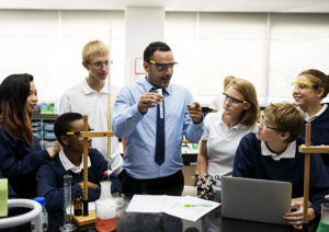 chemistry teacher holding a beaker and explaining to a room of students