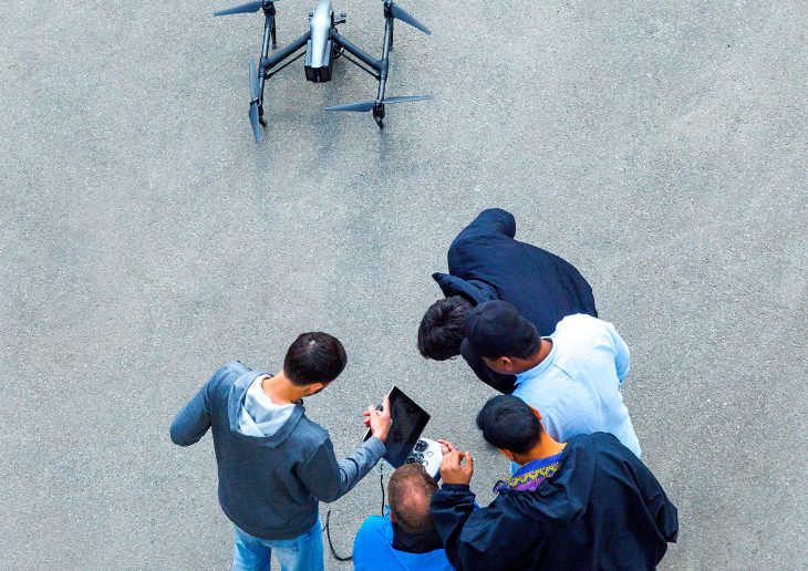 Students gathered around a drone control unit drone on the ground below them