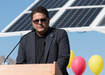 regional director jon caffery at a podium in front of huge solar panels