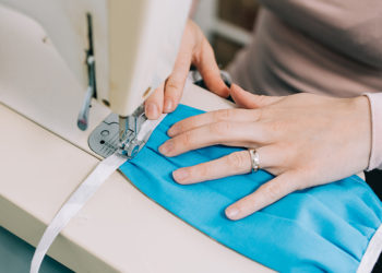 woman's hands on a sewing machine stitching a covid face mask