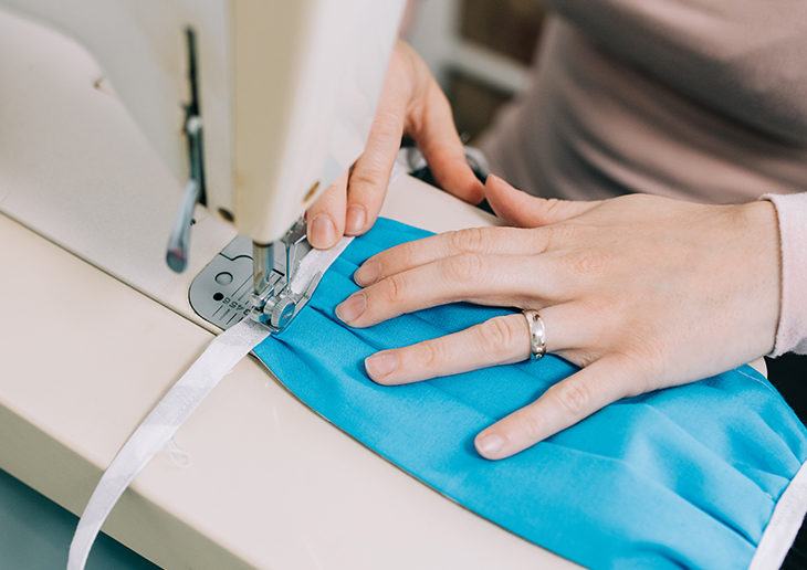woman's hands on a sewing machine stitching a covid face mask