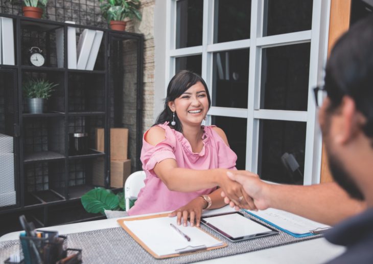 Hispanic business woman at a desk shaking a man's hand
